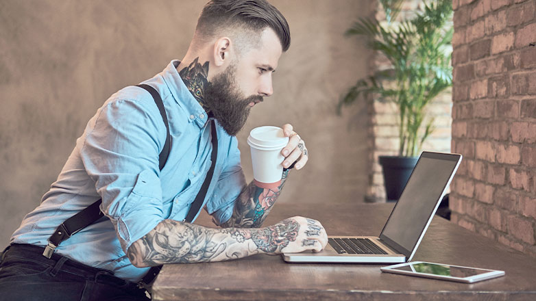 man drinking coffee seriously looking at laptop on desk