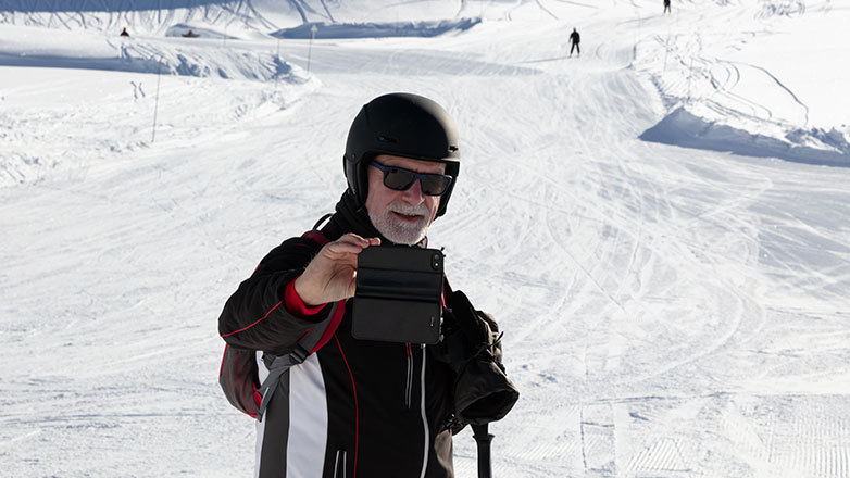 Older man taking a selfie at the bottom of a ski hill.