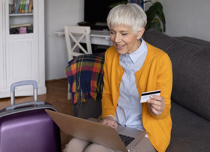 Elderly woman books a flight online using her credit card.
