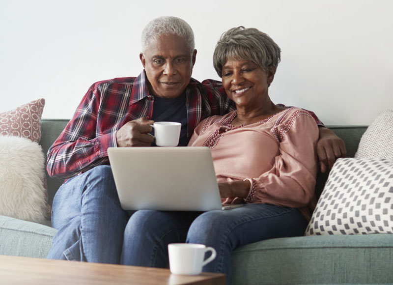 Senior couple sitting on couch together and looking at a laptop screen.